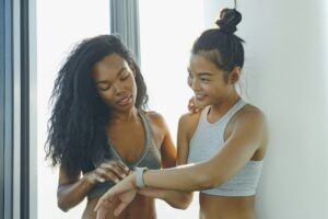 Two young women in gym, looking at activity tracker